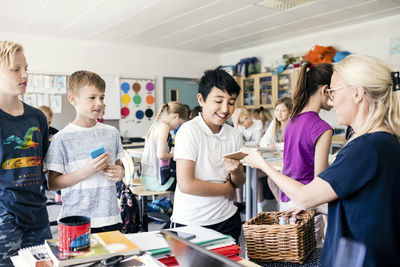 Teacher giving mobile phone to student at classroom