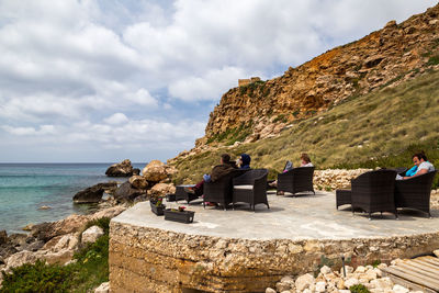 People on rock by sea against sky