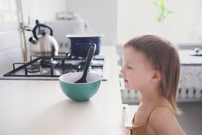 Cute toddler child in kitchen by stove helps mom cook, bright interior of kitchen