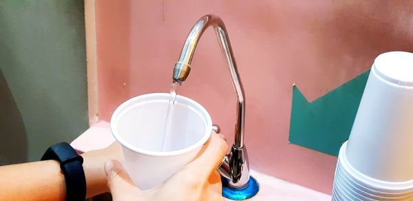 Cropped hands of person filling water in disposable cup