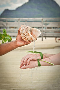 Cropped man with seashell pouring water on couple hands