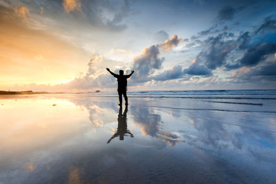 Silhouette man standing on shore at beach against sky during sunset