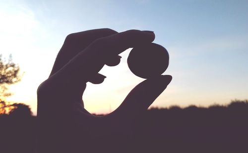 Close-up of silhouette hand holding sun against sky during sunset