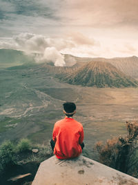 Rear view of man sitting on mountain against sky