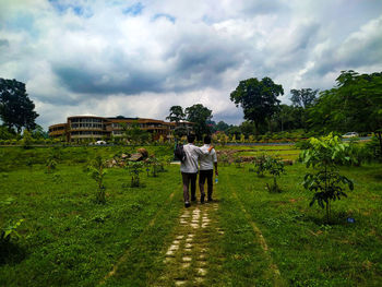 Rear view of people walking on field against sky