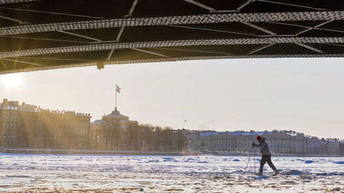 Silhouette of skier riding on ice of frozen neva river under the palace bridge in winter at sunset