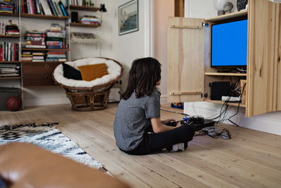 Side view of boy playing video game while sitting on hardwood floor at home