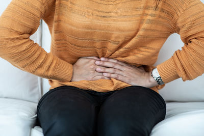 Midsection of woman with stomachache sitting at home