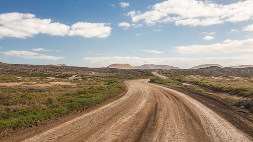 Dirt road amidst landscape against sky