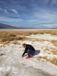 Mature woman crouching on sand against sky