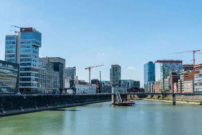 Bridge over river by buildings in city against sky