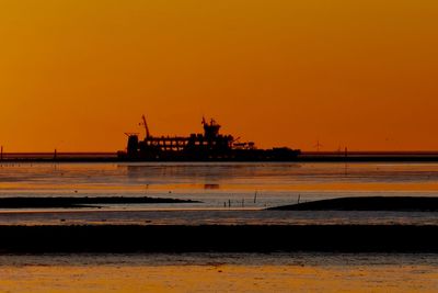 Silhouette cranes at sea against sky during sunset