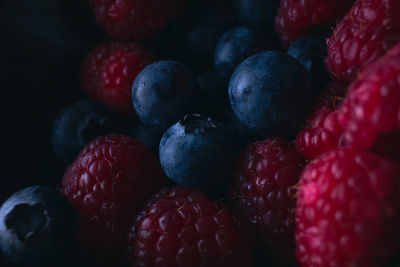 High angle view of fresh raspberries and blueberries in low light.