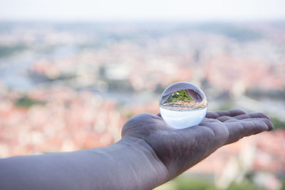 Cropped hand of woman holding crystal ball against townscape