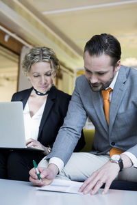 Mature businesswoman looking at male colleague signing document in office