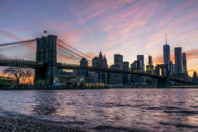 Brooklyn bridge over river with buildings in background at sunset