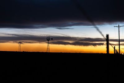 Silhouette of electricity pylon on field against sky at sunset