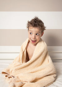 Cheerful boy wrapped in towel on bed