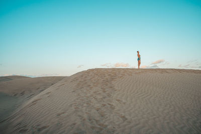 Rear view of man walking on beach against clear sky
