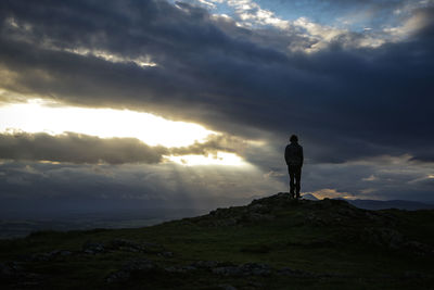 Man standing on rock against sky during sunset