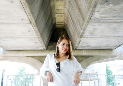 Portrait of young woman standing against bridge