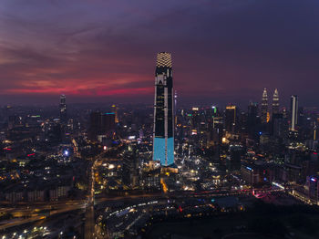 Illuminated modern buildings in city against sky at night