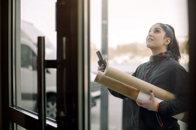 Young delivery woman with package at entrance of house