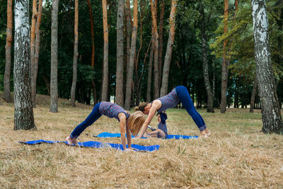 Family fitness and yoga. happy mom exercising with baby girls on grassy land against trees in