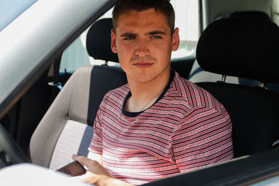 Serious successful caucasian young man sitting in car. 20s guy looking from open window. silver grey 