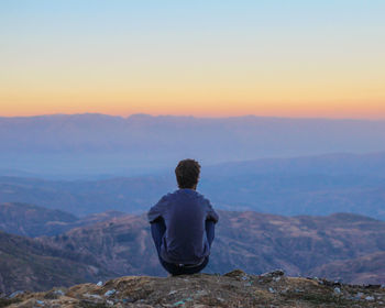 Rear view of man standing on mountain against sky during sunset