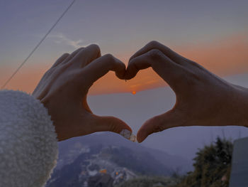 Midsection of heart shape against sky during sunset