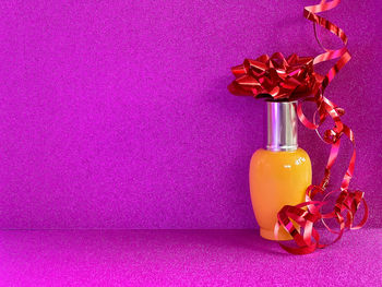 Yellow glass toiletries bottle with red rosette and red ribbons on purple glittery background.