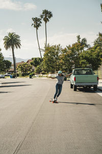 Woman with arms outstretched skateboarding on road against sky during sunny day