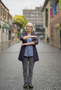 Full length portrait of woman gesturing while standing on footpath against buildings