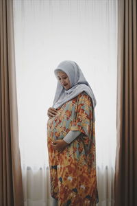 Pregnant woman touching belly while standing at home