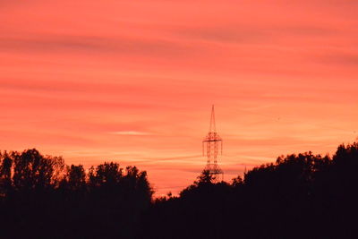 Silhouette trees and electricity pylon against sky during sunset