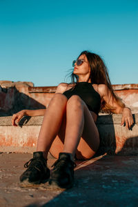 Beautiful young woman sitting in park against clear sky