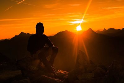 Man sitting on mountain against sky at sunset