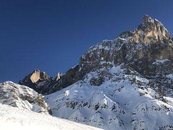 Low angle view of snowcapped mountains against clear blue sky