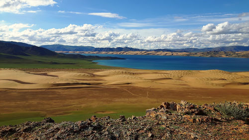 Scenic view of sandy landscape with a stunning blue mongolian lake against the sky