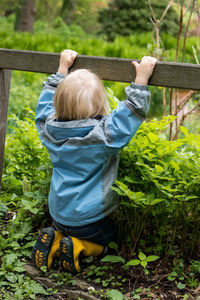 Rear view of boy with arms raised in plants