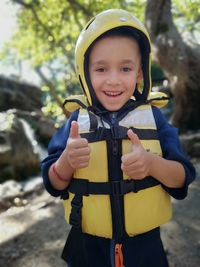 Portrait of smiling boy showing thumbs up while standing in forest