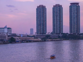 Modern buildings by river against sky in city