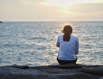Man sitting on shore against sea during sunset