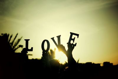 Silhouette people holding love alphabets at sunset