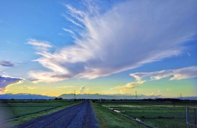 Empty road amidst field against sky during sunset