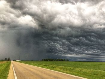 Road passing through field against cloudy sky