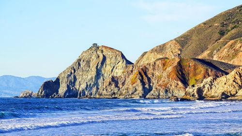 Scenic view of sea by mountain against sky