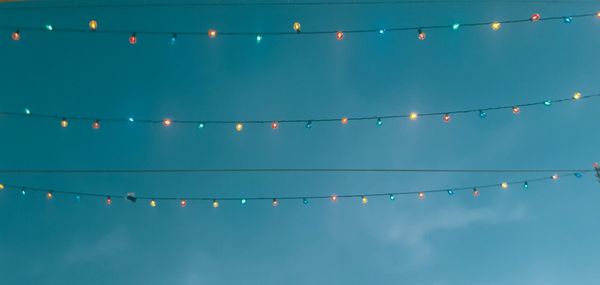 Low angle view of illuminated light bulbs hanging against blue sky during dusk