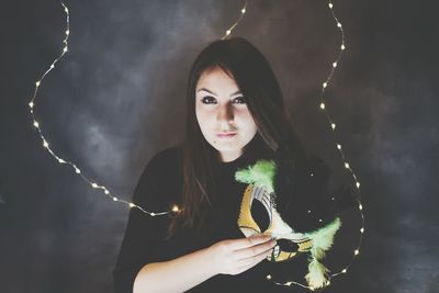 Portrait of young woman holding mask against illuminated lights